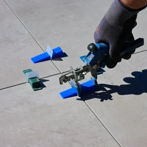 A gloved hand using a leveling tool to install tiles with spacers.